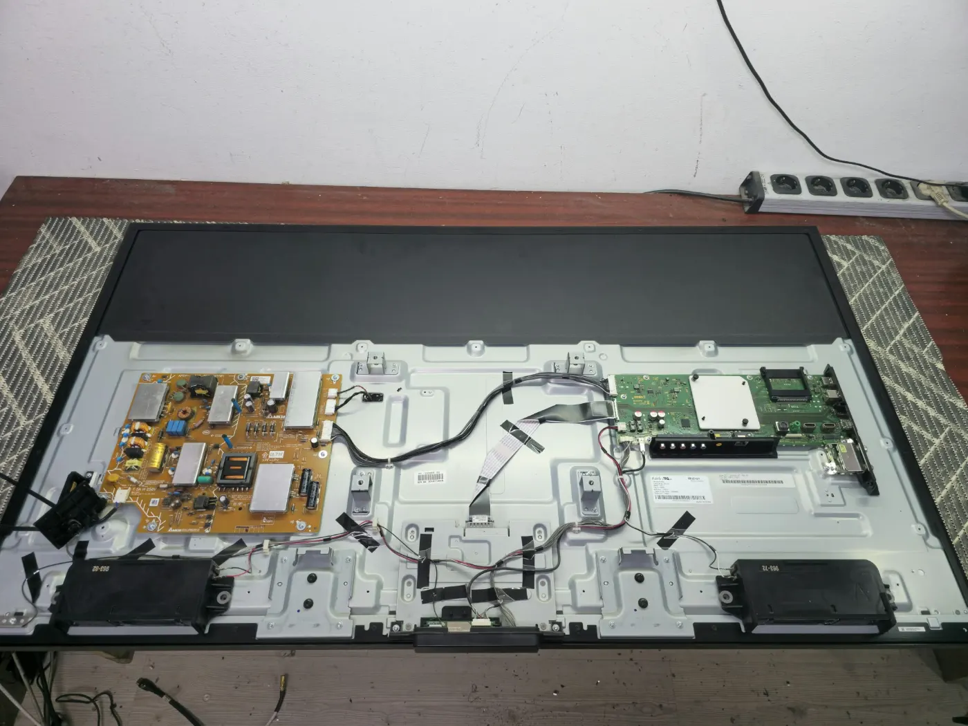Televizor Sony KD-55XE8096 desfăcut pe bancul de lucru: sursa de alimentare în stânga, placa de bază în dreapta, difuzoarele jos